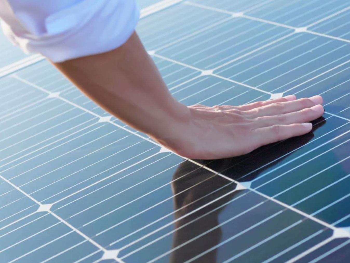Ruka dotýkající se fotovoltaických modulů. 