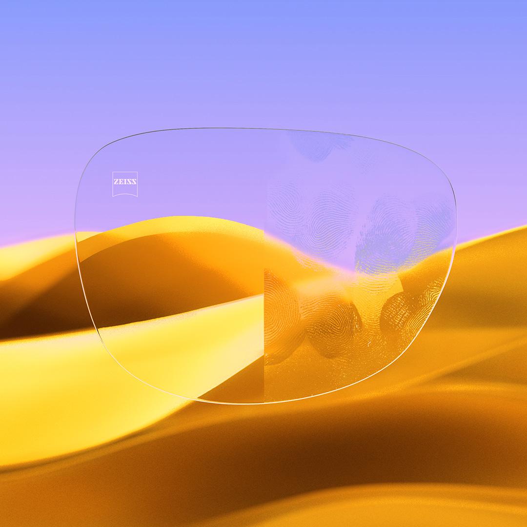 Rozdělená brýlová čočka s jednou stranou čistou a čirou, která je opatřena povrchovou úpravou ZEISS DuraVision Gold UV, a druhou stranou s otisky prstů.