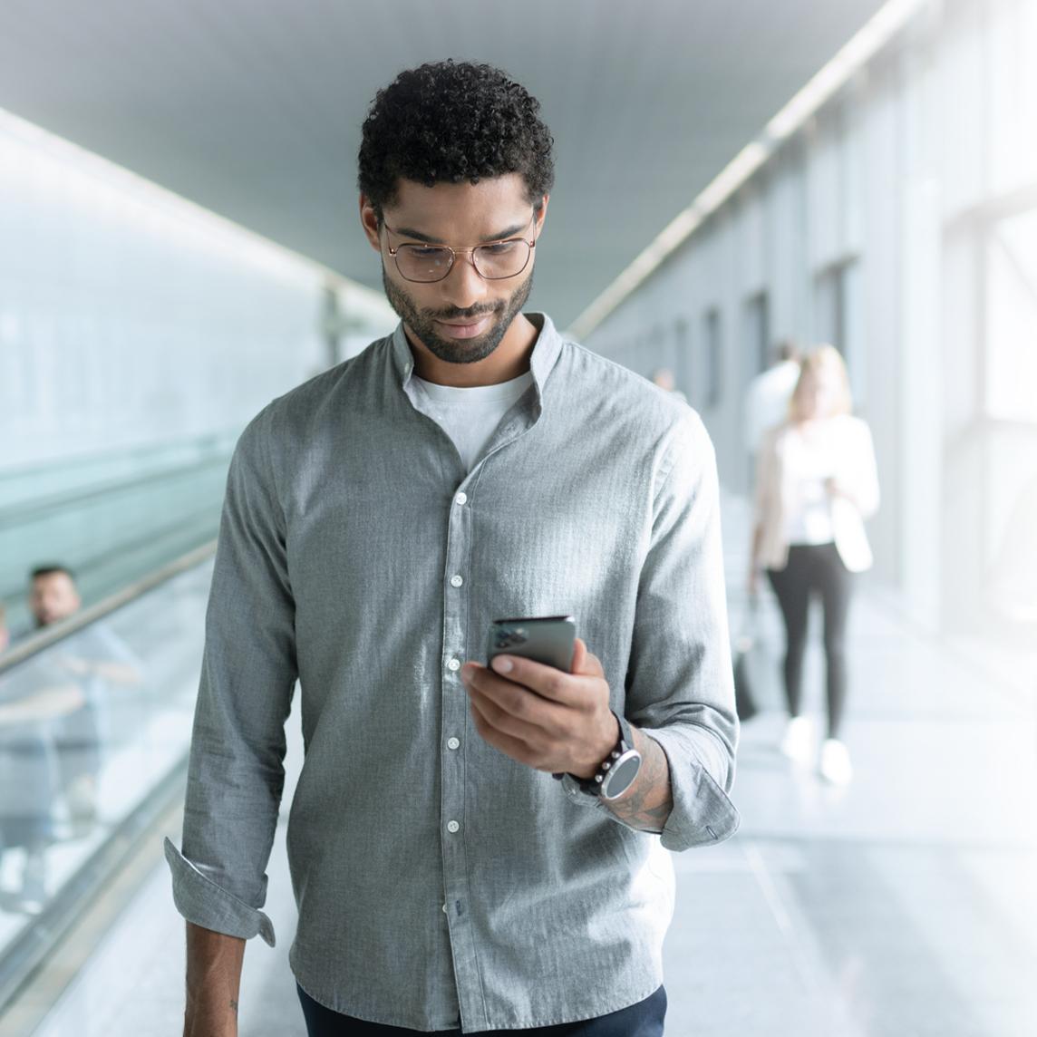 Mladý muž v brýlových čočkách ZEISS SmartLife se při chůzi dívá do telefonu.