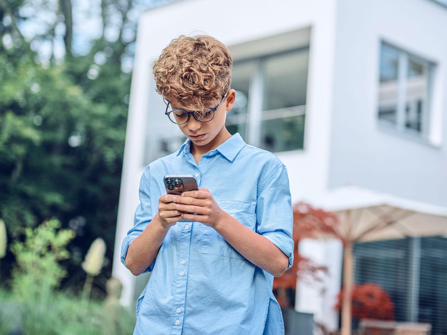 Mladý chlapec se venku dívá na mobilní telefon.