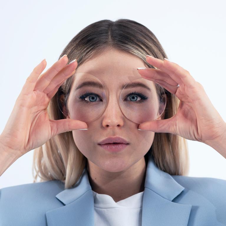 Mladá blondýna drží před očima čočky, přes které je díky jednoohniskovým čočkám ZEISS ClearView vidět dobře a bez zkreslení.
