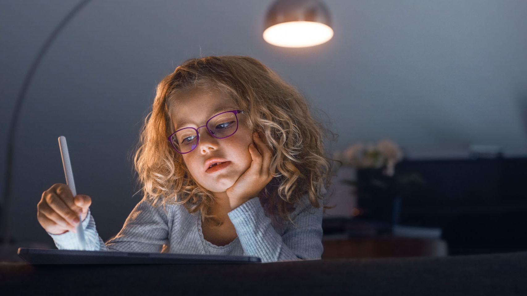 Malá dívka v tmavém obývacím pokoji se dívá na tablet.