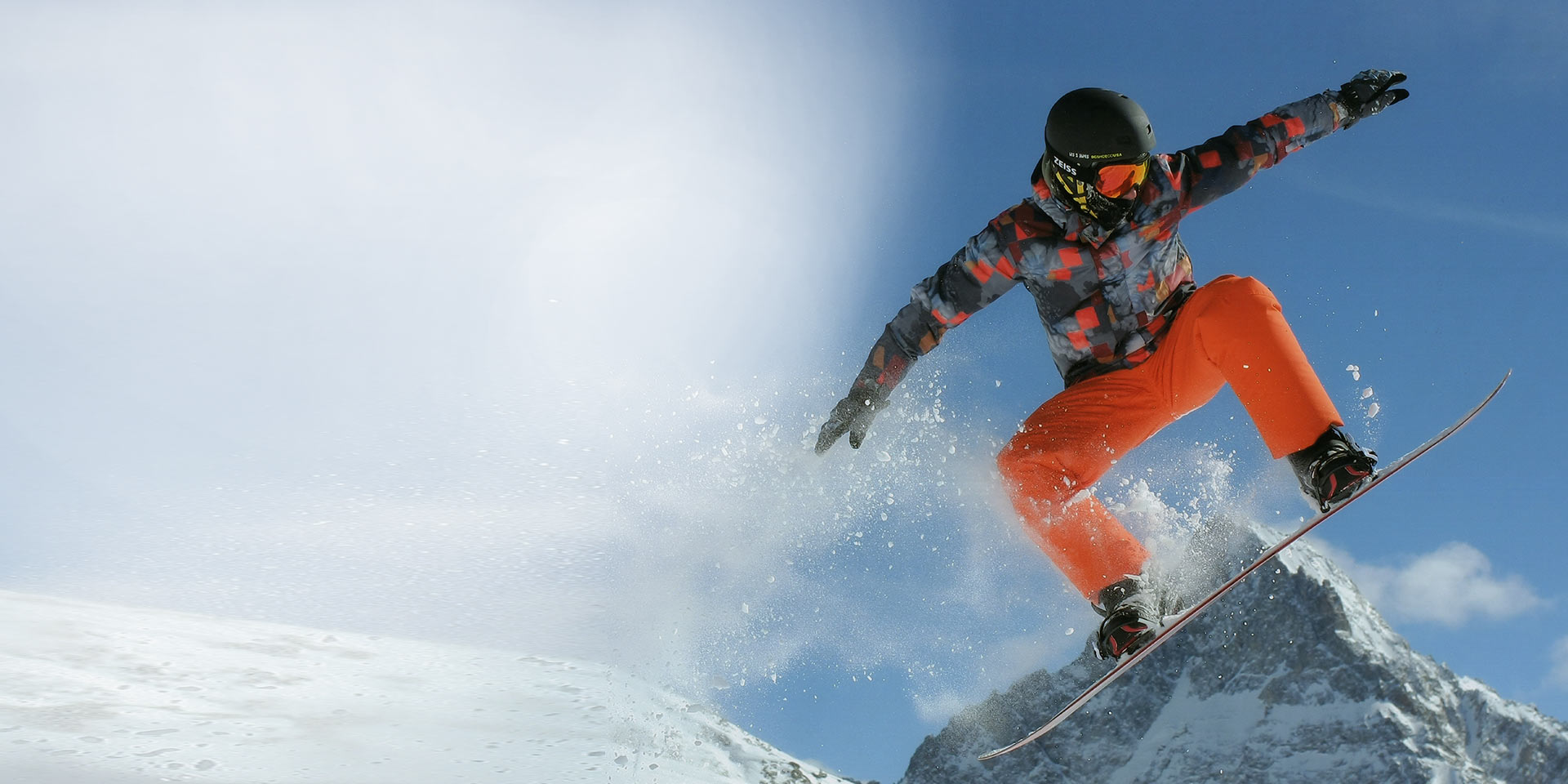 Muž skáče na snowboardu a má nasazenou černou snowboardovou přilbu a ZEISS lyžařské brýle, které umožňují výměnu skel, pro maximální ochranu