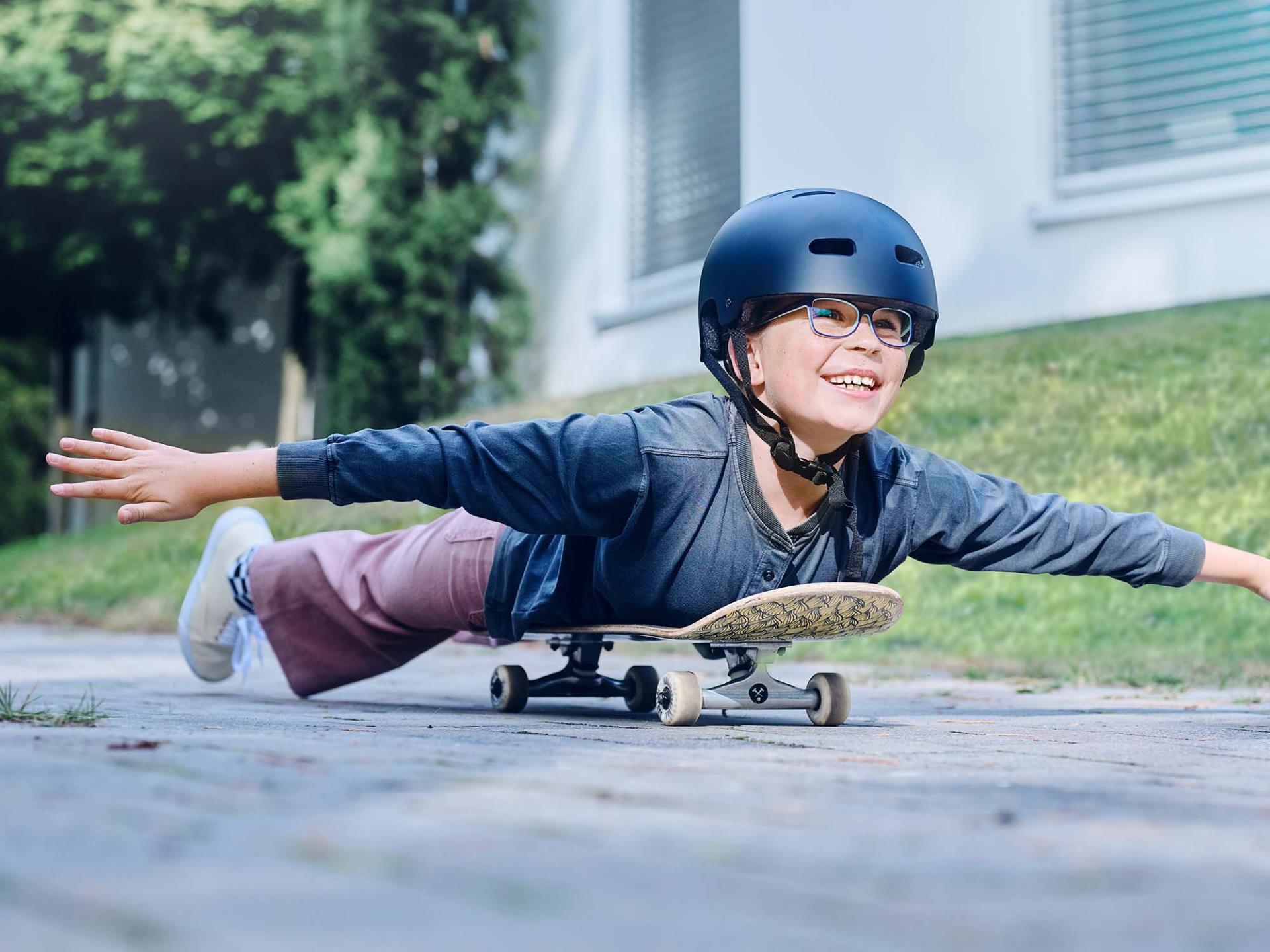 Dívka s helmou a brýlemi se řítí na skateboardu po silnici a natahuje ruce.