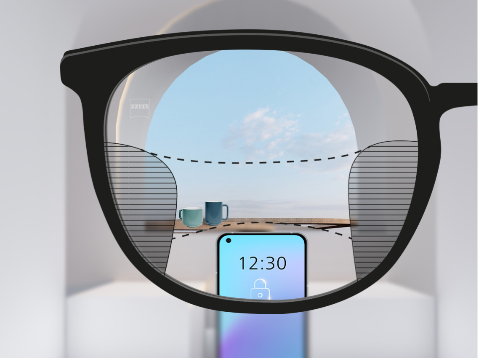 Obrázek zorného pole s brýlovými čočkami ZEISS Progressive SmartLife, přes které je ostře vidět chytrý telefon s pohárky v pozadí, nalevo a napravo jsou vidět úzké plochy.
