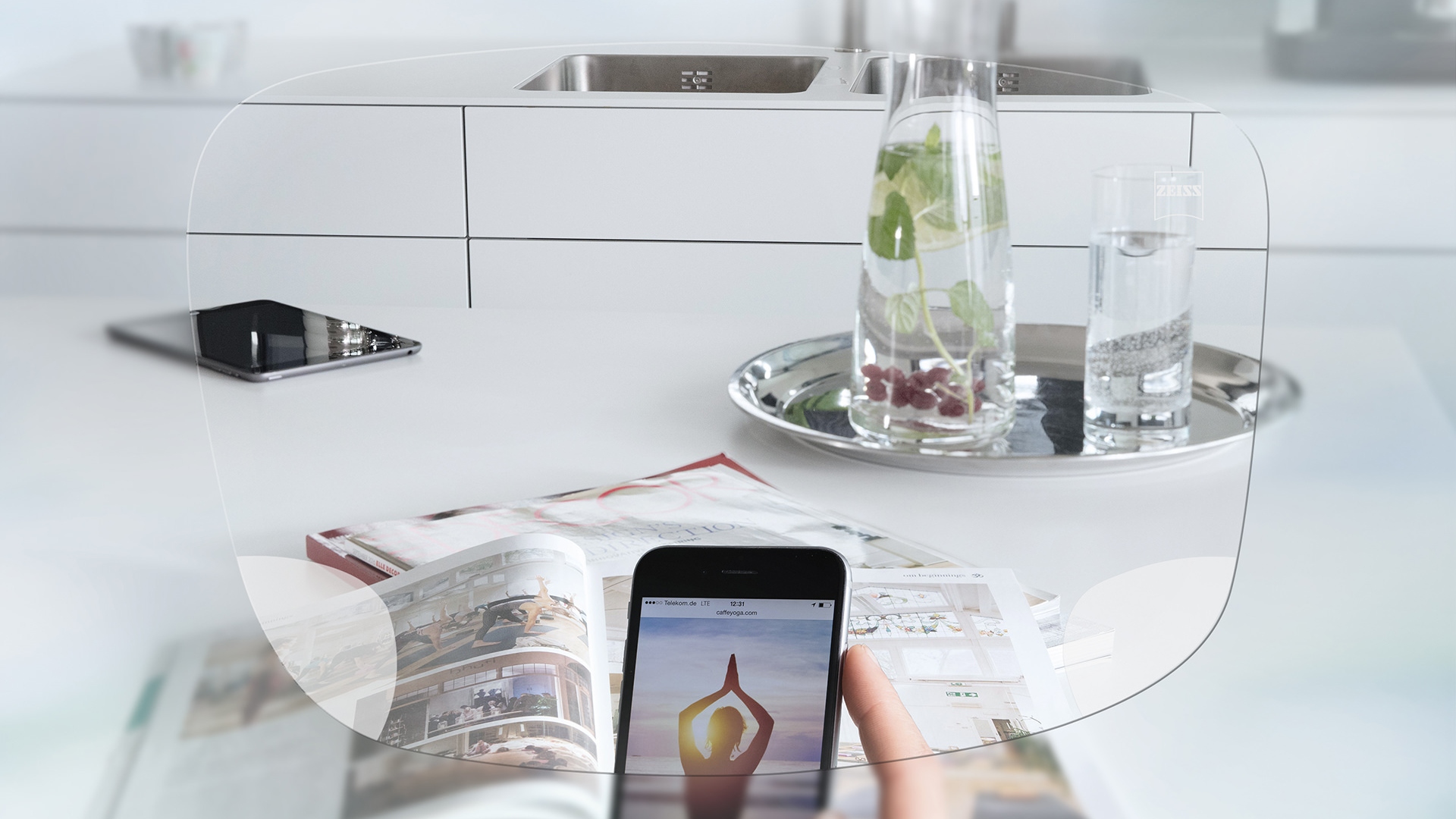 Pohled přes jednoohniskové brýlové čočky ZEISS EnergizeMe na obrazovku chytrého telefonu a uspořádaný kuchyňský stůl.