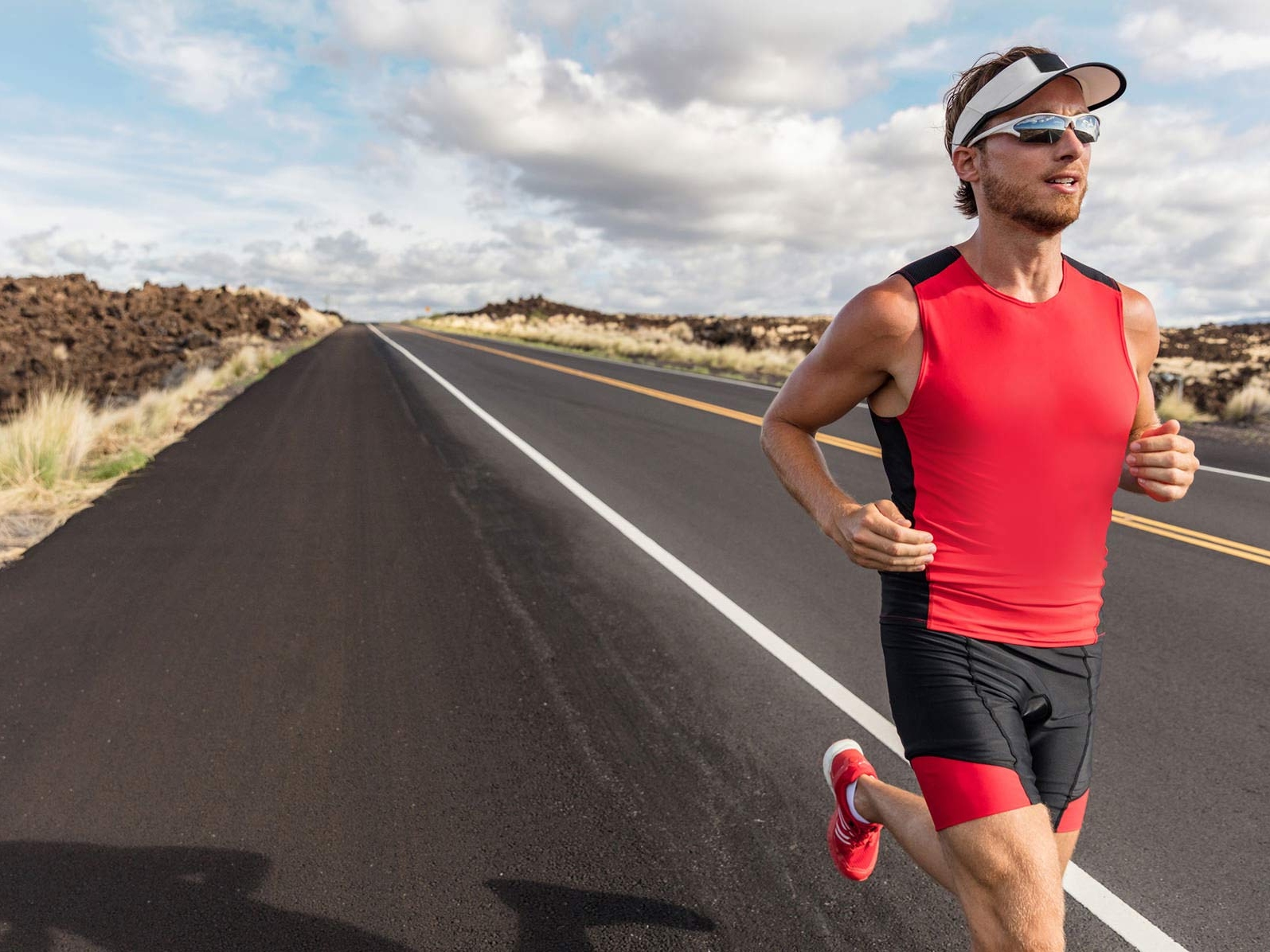 Obrázek sportovně oblečeného muže se sportovními brýlemi, zatímco běží po cestě z kopce. 