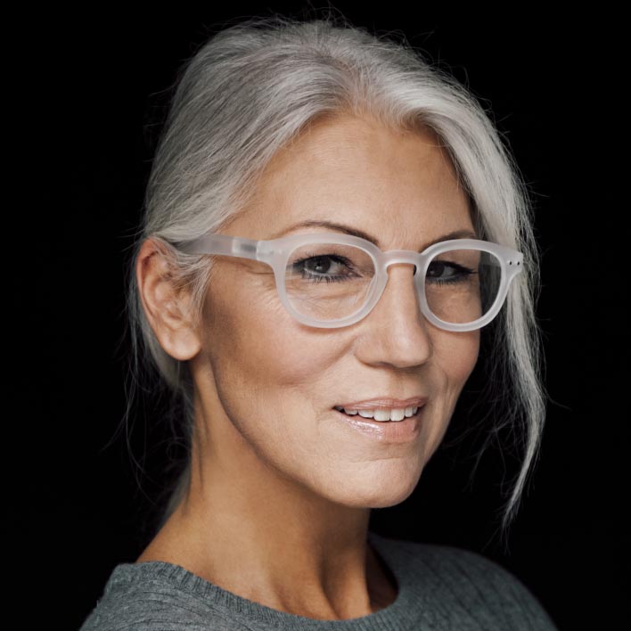 Žena s šedými vlasy má na sobě brýle s bílými obrubami a progresivními čočkami ZEISS SmartLife. Geometrický sken obličeje zobrazující anatomii obličeje a naměřené hodnoty obrub.